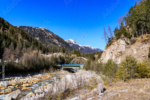 Mountain bridge crossing alpine river in early spring landscape..