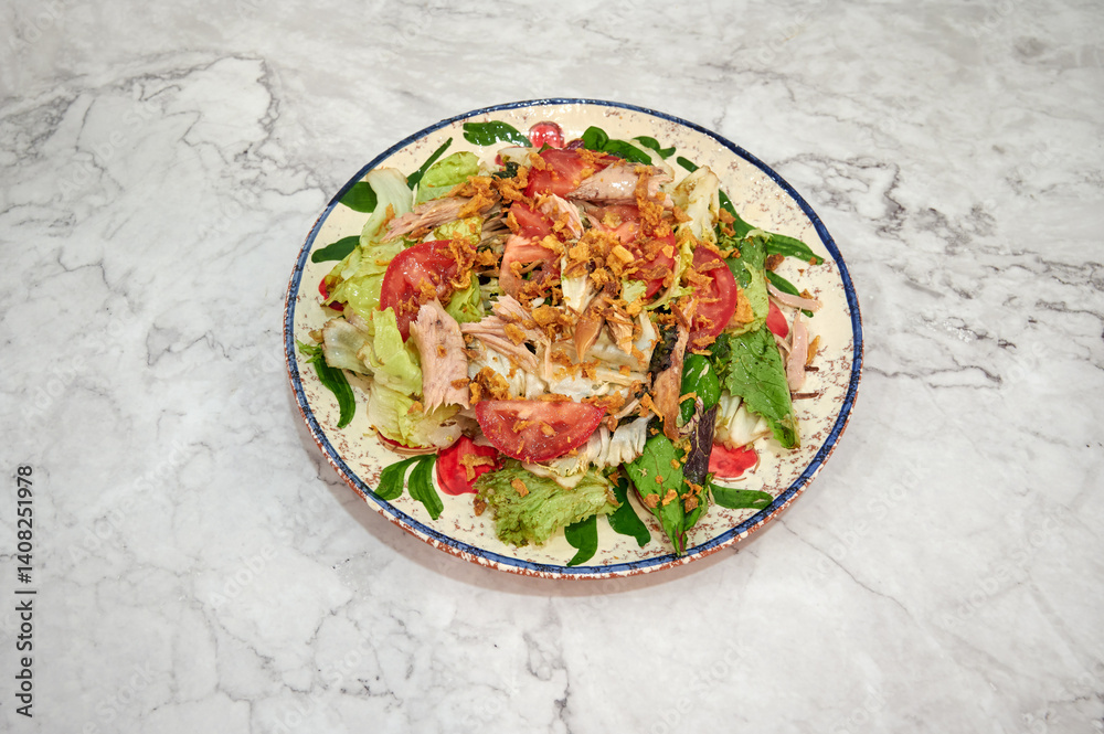 A salad with lettuce, tomatoes, and chicken on a white plate. The plate is on a marble counter