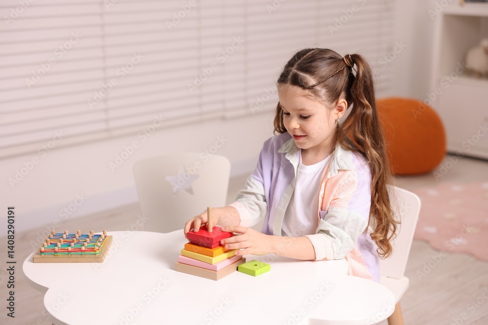 Motor skills development. Little girl playing with toy pyramid at white table indoors Motor skills development. Little girl playing with toy pyramid at white table indoors