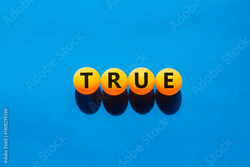 True symbol. Concept word True on beautiful yellow ping pong balls. Beautiful blue table blue background. Business, lifestyle, support and true concept. Copy space.