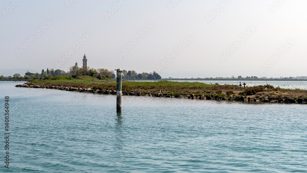 Peaceful view of Barbana Island from the water, with its iconic church and towers emerging through the lagoon’s calm reflections. Peaceful view of Barbana Island from the water, with its iconic church and towers emerging through the lagoon’s calm reflections.