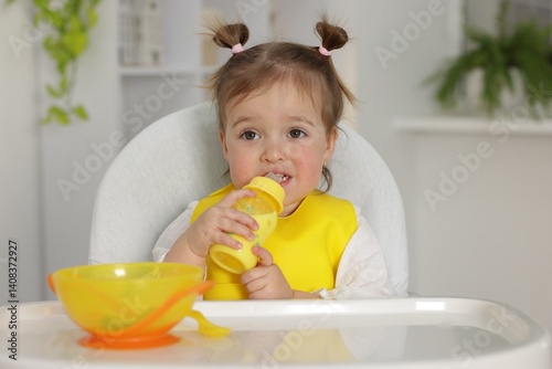 Little baby feeding from bottle in high chair at home