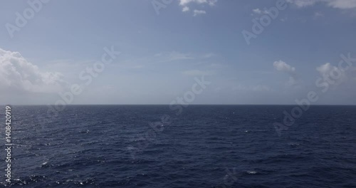 4k 19 second video clip footage of ocean surface wake coming from cruise ship panning up to horizon and cloudy blue sky.