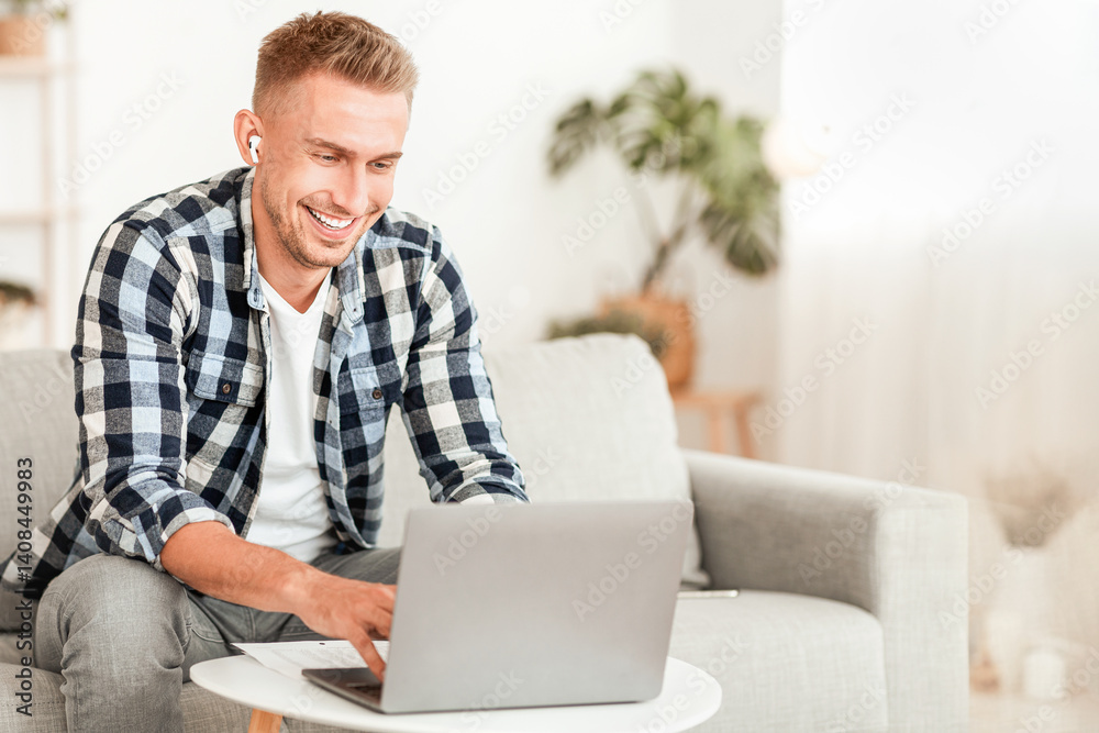 Education Concept. Cheerful guy studying online using laptop sitting on couch and wearing earbuds, copy space Education Concept. Cheerful guy studying online using laptop sitting on couch and wearing earbuds, copy space