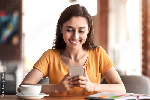 Happy girl sitting at cafe, drinking tea and using smartphone, looking for part-time job, copy space