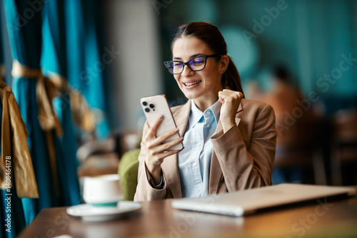 Portrait of overjoyed lady sitting in cafe, smiling at cellphone and celebrating victory and success