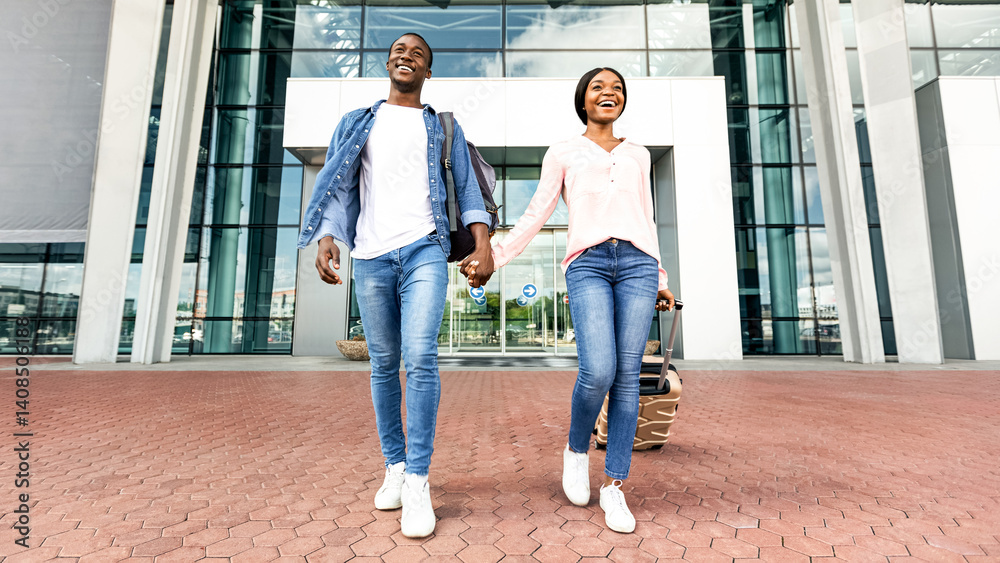 Fototapeta premium Ready For Adventures. Excited Black Couple Leaving Airport Building In New Country, Enjoying Travelling Together, Holding Hands