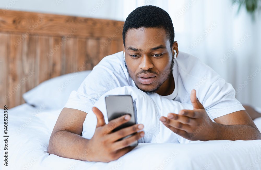 Serious African American Man Making Video Call On Smartphone Lying In Bed At Home. Distant Online Communication, Video Conference Mobile Application Concept. Selective Focus Serious African American Man Making Video Call On Smartphone Lying In Bed At Home. Distant Online Communication, Video Conference Mobile Application Concept. Selective Focus