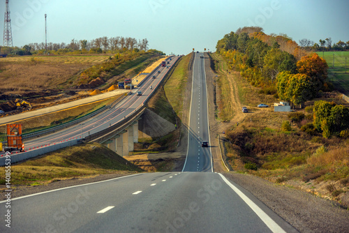 a section of highway running along a hill. On the left, construction or widening work can be seen - machinery, sand embankments and temporary barriers.  