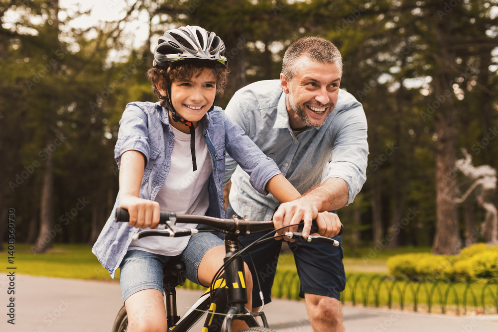 Having Fun. Laughing parent teaching son how to ride a bicycle at public park Having Fun. Laughing parent teaching son how to ride a bicycle at public park