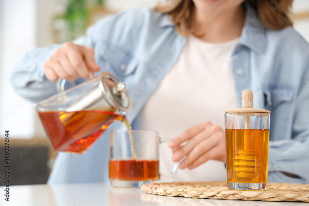 Jar of tasty honey on table and woman pouring tea in kitchen Jar of tasty honey on table and woman pouring tea in kitchen