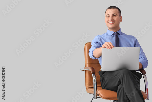 Handsome businessman with laptop in chair on light background