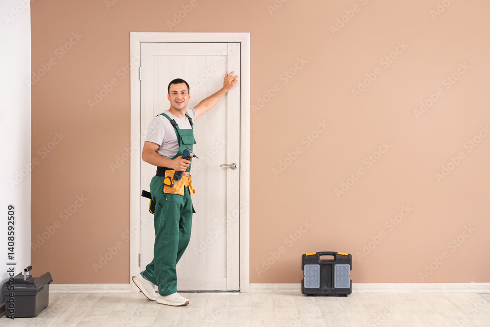 Male worker with electric drill near door at home