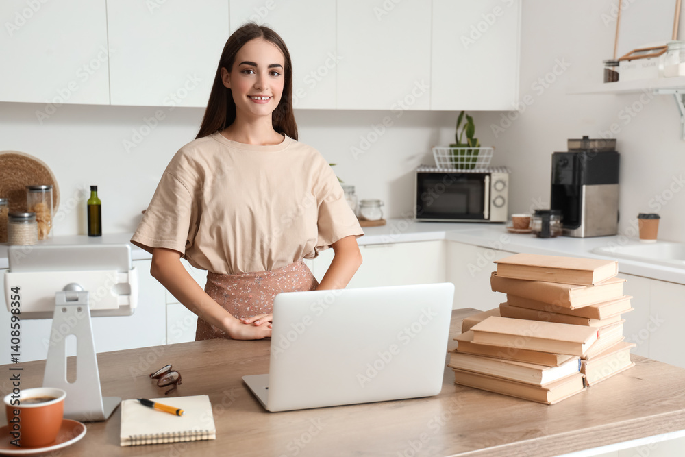Happy female student with laptop, tablet and books studying in kitchen Happy female student with laptop, tablet and books studying in kitchen
