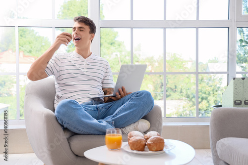 Young man with laptop eatin...