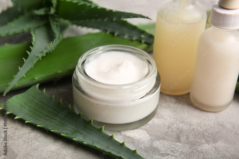 Bottles of cosmetic oil and jar of cream with aloe vera leaves on grey background, closeup