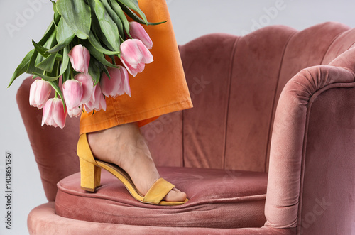 Obraz na płótnie Leg of woman in high heels with tulips on armchair against light background w salonie