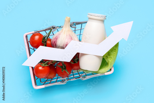 Shopping basket with products and arrow on blue background. Concept of rising price