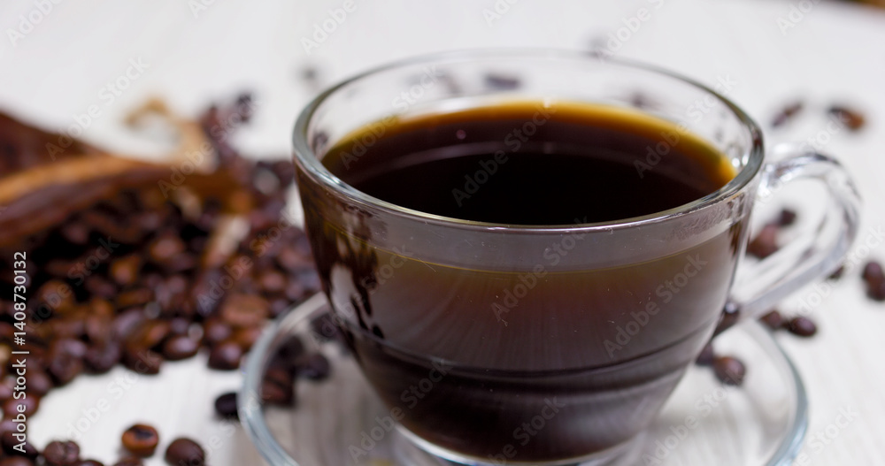 Steaming cup of black coffee sits on a glass saucer, surrounded by roasted coffee beans on a light wooden table, creating a cozy and aromatic scene Steaming cup of black coffee sits on a glass saucer, surrounded by roasted coffee beans on a light wooden table, creating a cozy and aromatic scene