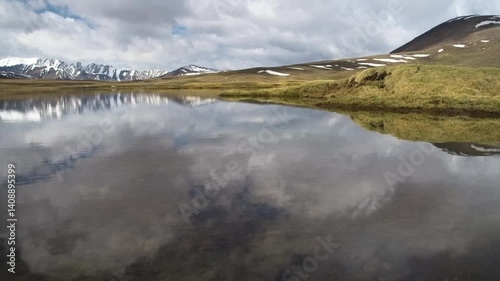 Footage shows a picturesque lake reflecting the sky, surrounded by majestic mountains in the Ural Mountains region of Kyrgyzstan.
