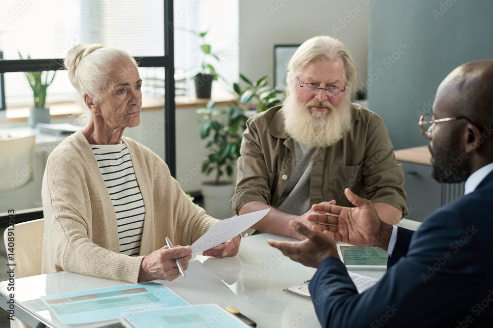 Senior couple discussing mortgage agreement with real estate agent at meeting in office