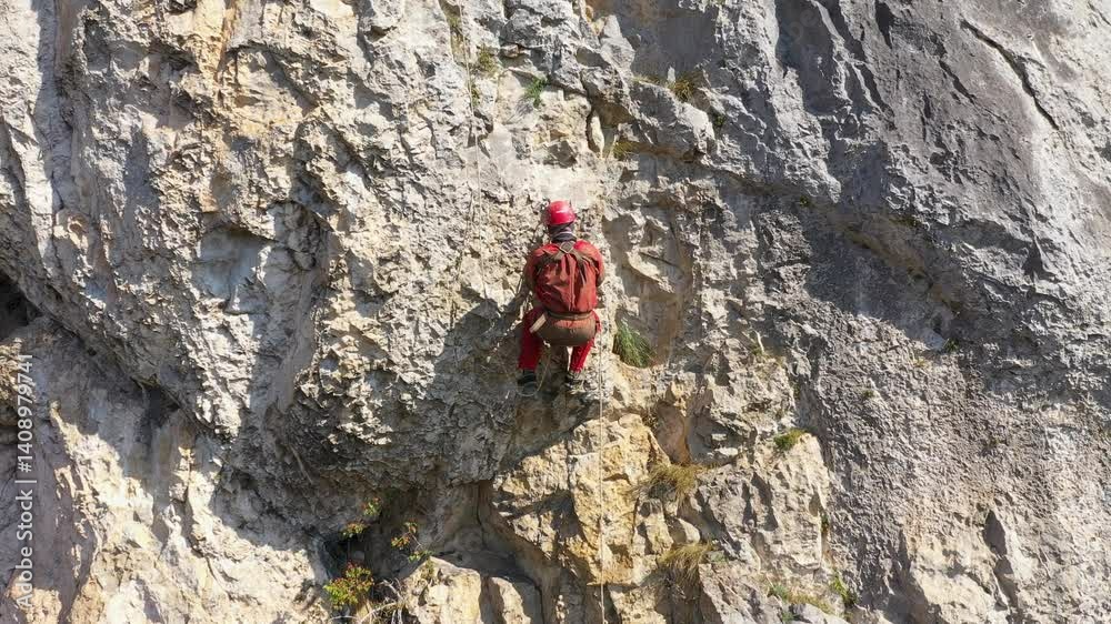 Aerial view of mountain rescuer rappelling on a rocky wall hanging on a rope Aerial view of mountain rescuer rappelling on a rocky wall hanging on a rope