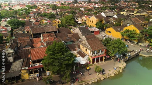 Tourists crossing historic japanese bridge spanning thu bon river, surrounded by colorful heritage buildings in hoi an's ancient unesco listed townscape
