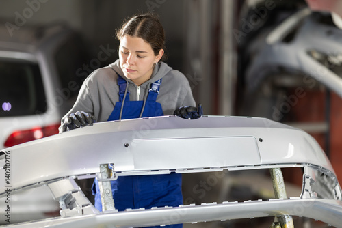 Obraz na płótnie Female auto mechanic checks the quality of painting of a car bumper in a car service w salonie