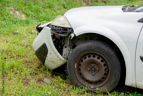 Obraz na płótnie Abandoned car is parked on a grassy terrain with significant damage to the front fender, exposing engine parts.. w salonie