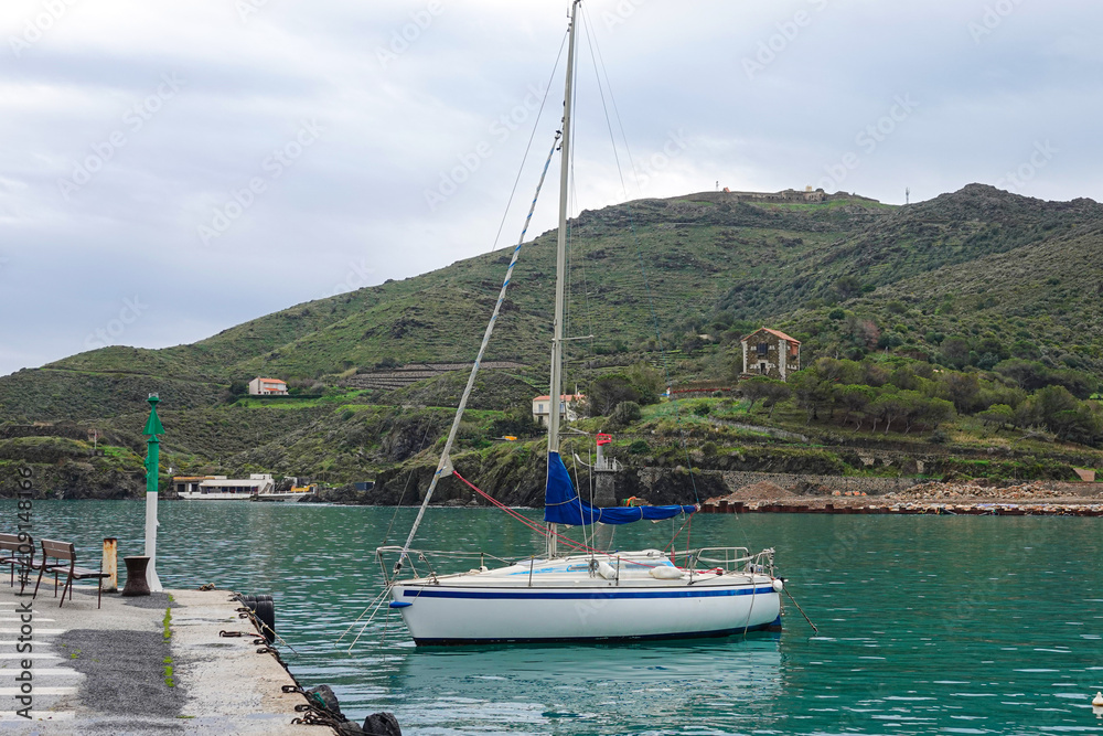 A sailboat rests peacefully at a dock surrounded by serene waters and lush green hills.,