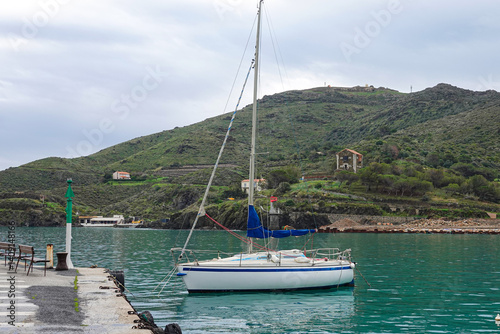 Obraz na płótnie A sailboat rests peacefully at a dock surrounded by serene waters and lush green hills., w salonie