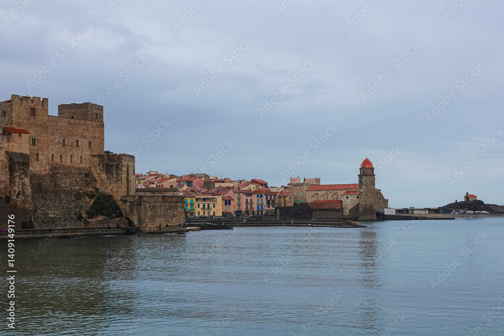 A historic castle stands prominently along the coast, with a charming town filled with colorful buildings in the background. Collioure, France