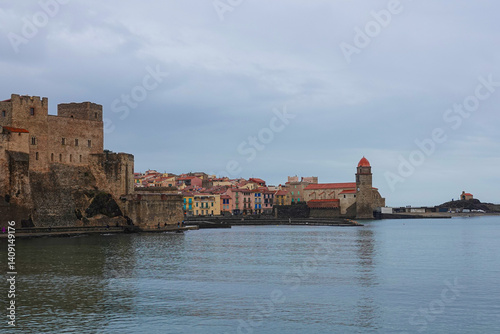 Obraz na płótnie A historic castle stands prominently along the coast, with a charming town filled with colorful buildings in the background. Collioure, France w salonie