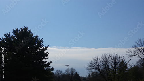 A thin layer of altostratus clouds blankets the sky, creating a hazy, diffused light. The blue is muted, softened by the veil of white, imparting a sense of calm and quietude to the scene.