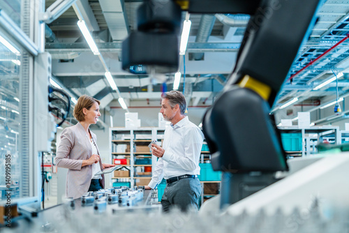 Two professionals discussing in a production hall with industrial robots