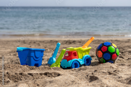 Bright colorful children's toys for sand on the beach, on the seashore. Ball, car, children's molds for sand. Building sandcastles and exploring the seashore with a plastic spoon. Summer Day.