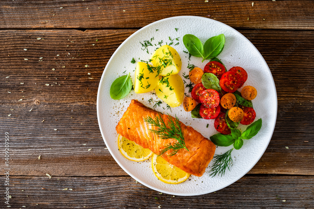 Seared salmon steak with cherry tomatoes and boiled potatoes on wooden table