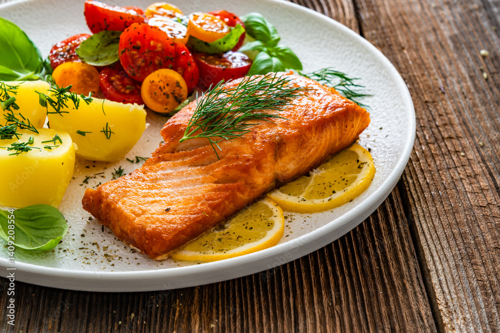Seared salmon steak with cherry tomatoes and boiled potatoes on wooden table