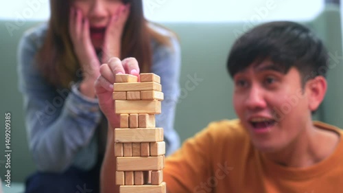 Happy asian diverse group friends playing together with wooden building blocks at home office sitting at the table enjoying time together. Office leisure and board games concept.