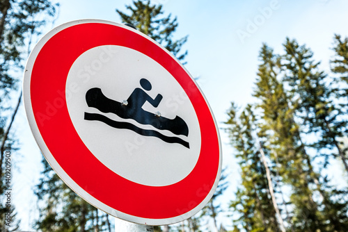 Sign indicating no canoeing allowed near a river surrounded by lush green forest during daylight hours