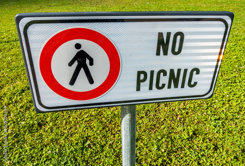 Sign forbidding picnics in a green park indicating restriction for pedestrians enjoying outdoor activities during a sunny day