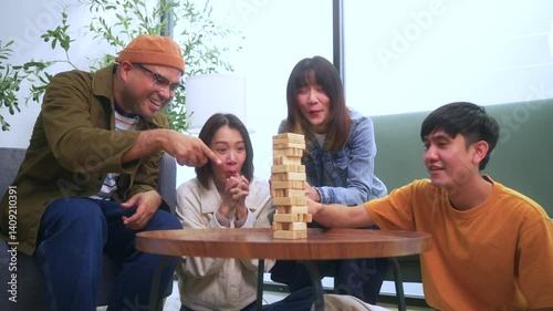 Happy asian diverse group friends playing together with wooden building blocks at home office sitting at the table enjoying time together. Office leisure and board games concept.