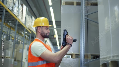 A man in a yellow hard hat and orange vest inspects a large package in a warehouse, ensuring quality and safety.