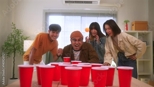 Happy asian diverse group friends playing together with beer pong at home office standing at the table enjoying time together. Office leisure and board games concept.