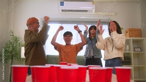 Happy asian diverse group friends playing together with beer pong at home office standing at the table enjoying time together. Office leisure and board games concept.