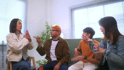 Happy asian diverse group friends together playing who am I game at home office sitting in the chair enjoying time together. Office leisure and board games concept.