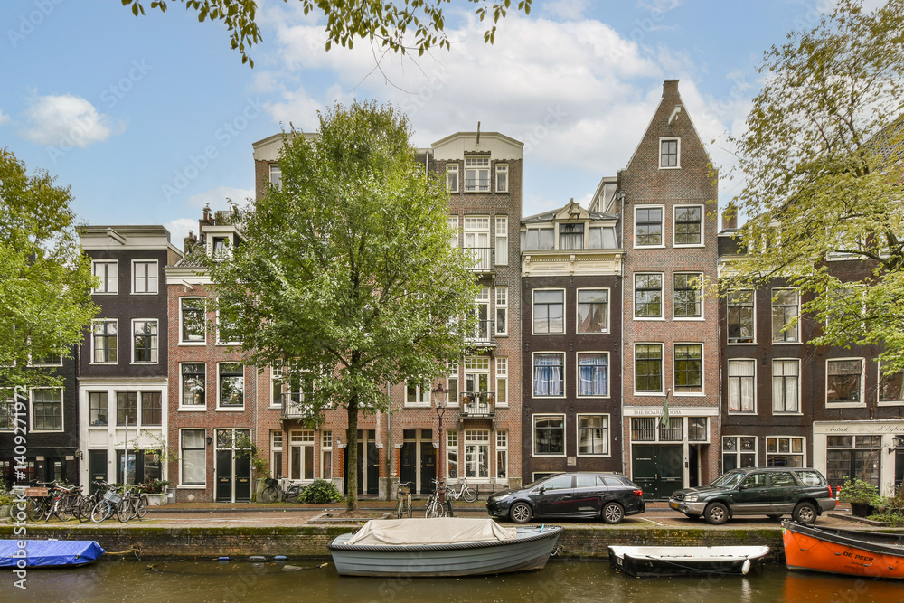 Obraz premium Quaint canal scene showcasing elegant architecture, flourishing trees, and boats nestled along the waterway, creating a picturesque view in Amsterdam.