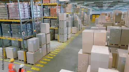 A bird's-eye view of a bustling warehouse reveals workers navigating aisles filled with stacked boxes and crates, highlighting the efficiency of logistics and storage management.