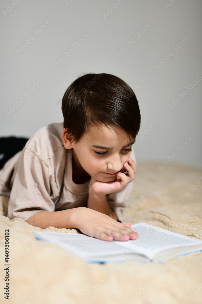 Little school boy reading a book lying on his bed Little school boy reading a book lying on his bed