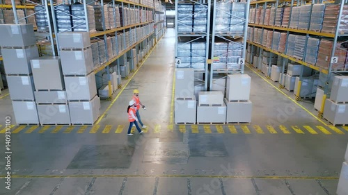 A bird's-eye view of a bustling warehouse reveals two workers navigating between towering shelves filled with crates and packages, highlighting the organized chaos of logistics and supply chain